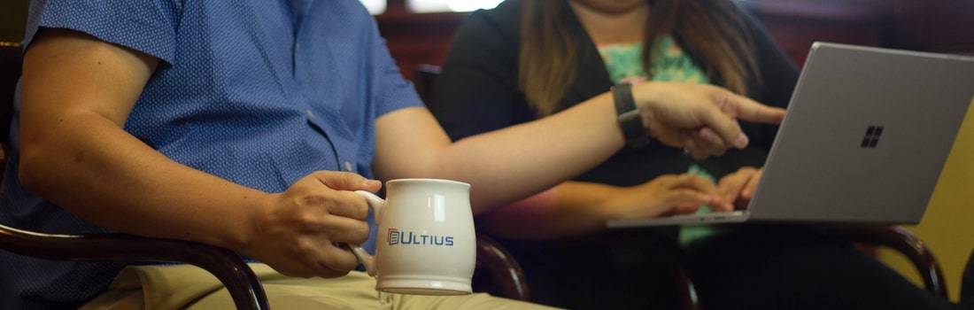 Holding an Ultius mug and pointing at a laptop