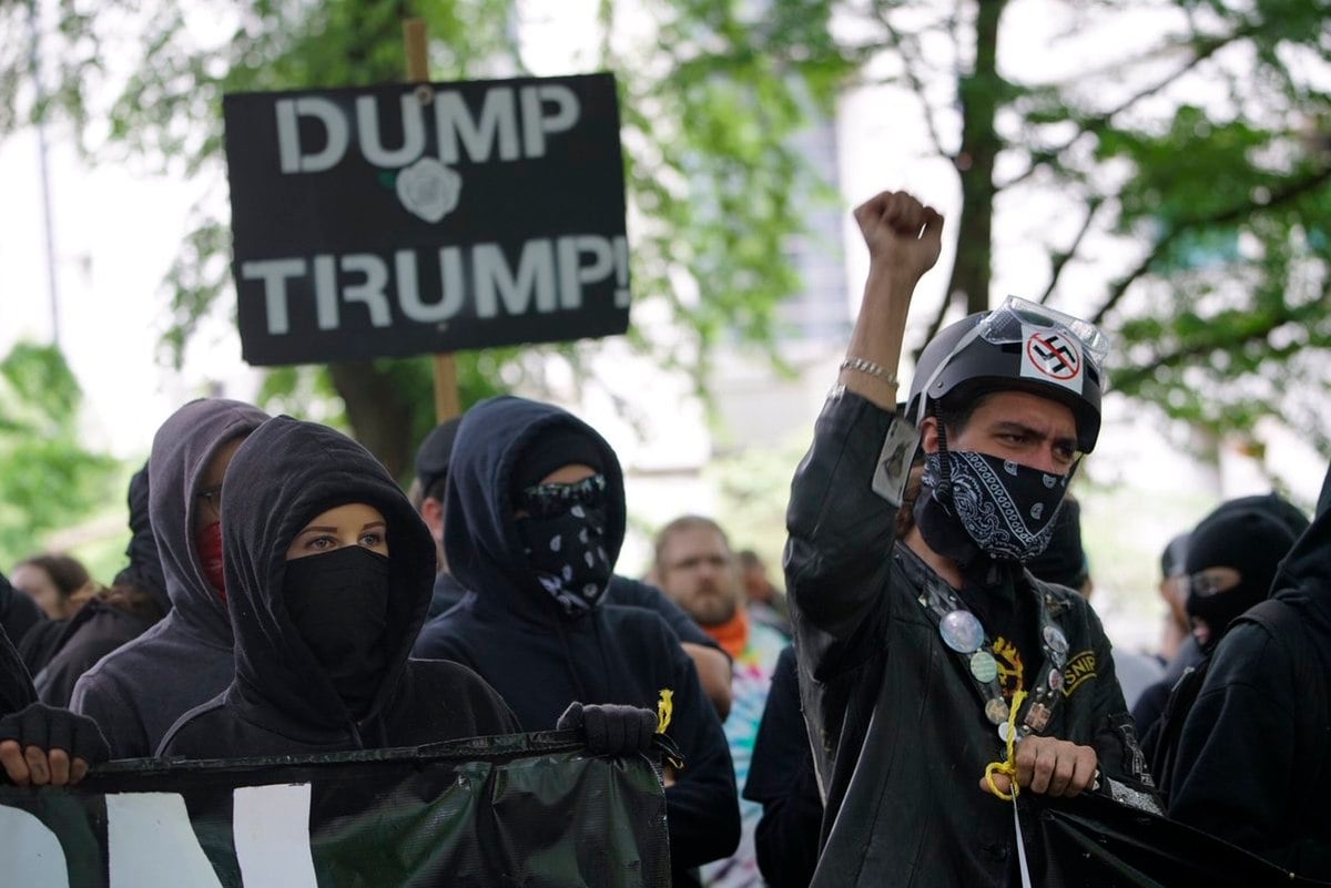Antifa members dressed in black, with a dump Trump sign